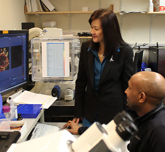 A seated man and two standing women look at a computer screen in a lab